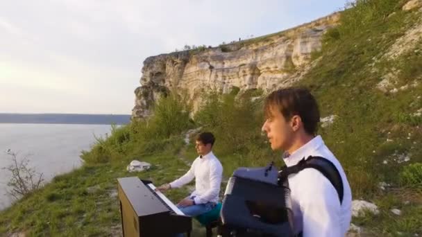 两个音乐家钢琴家和手风琴在海上日落打在岩石